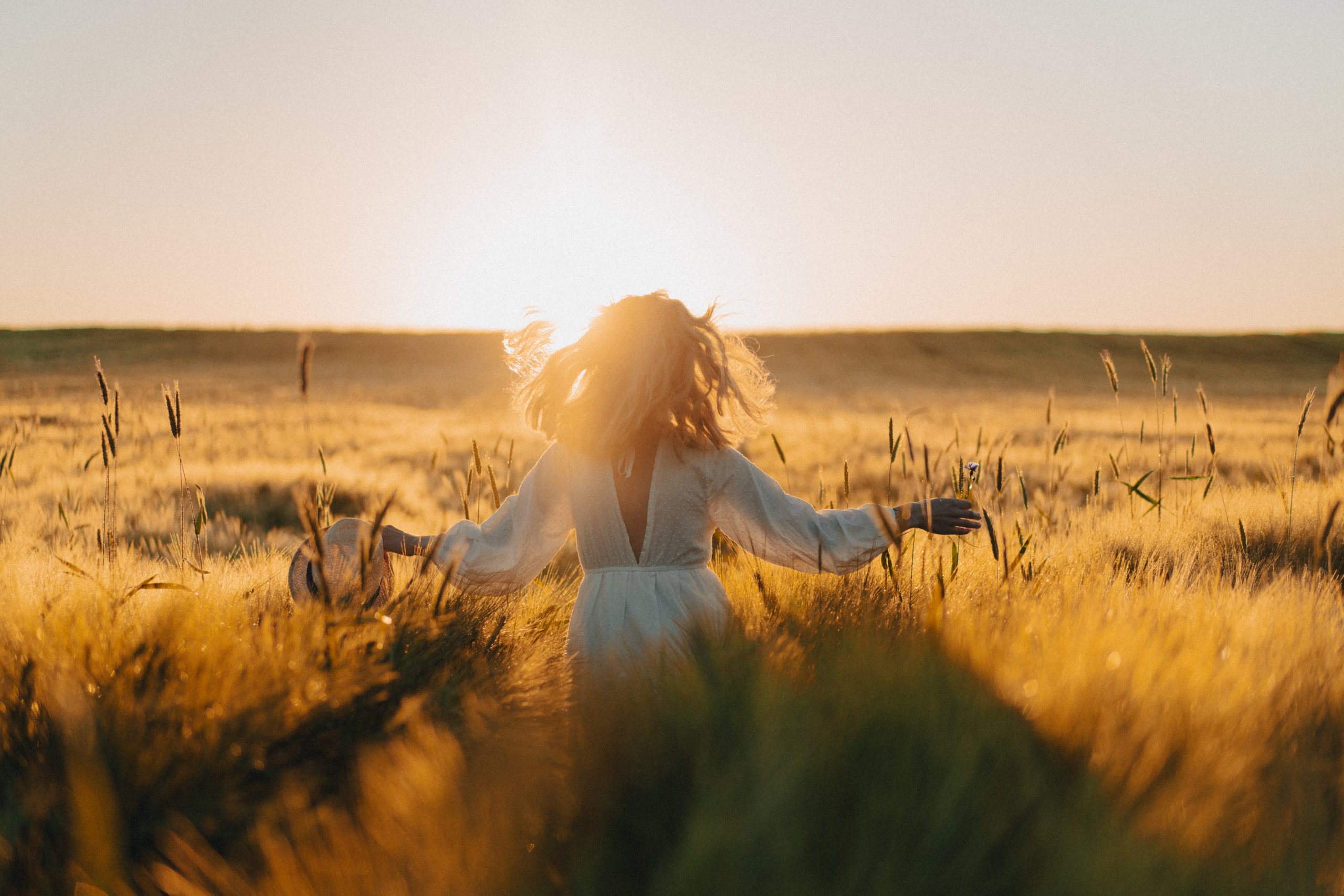 Thérapie de reconstruction après un deuil une femme les bras écarté, dans des hautes herbes, de dos regardant le coucher de soleil en face